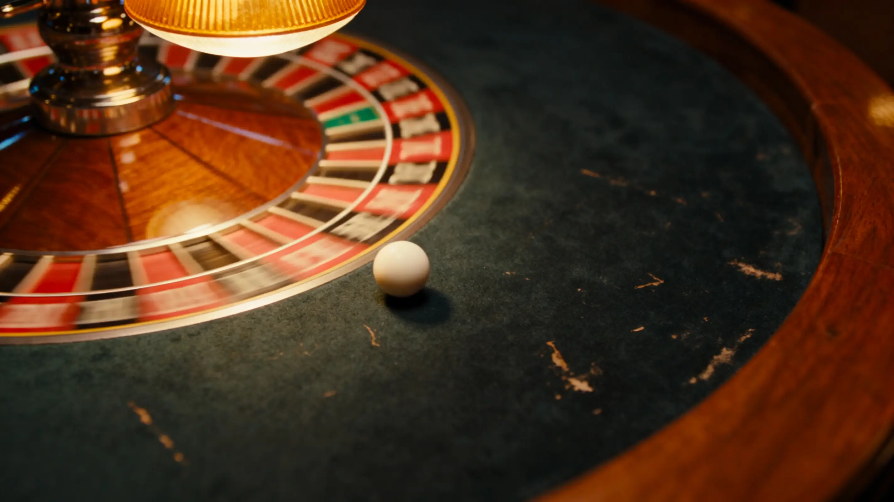 Roulette wheel spinning with white ball on green felt under warm lighting