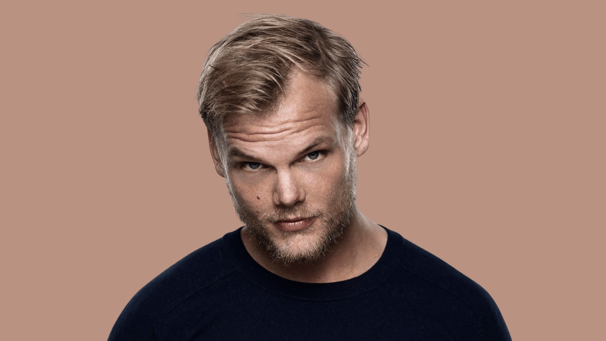 Close-up portrait of avicii in black shirt against muted beige background.
