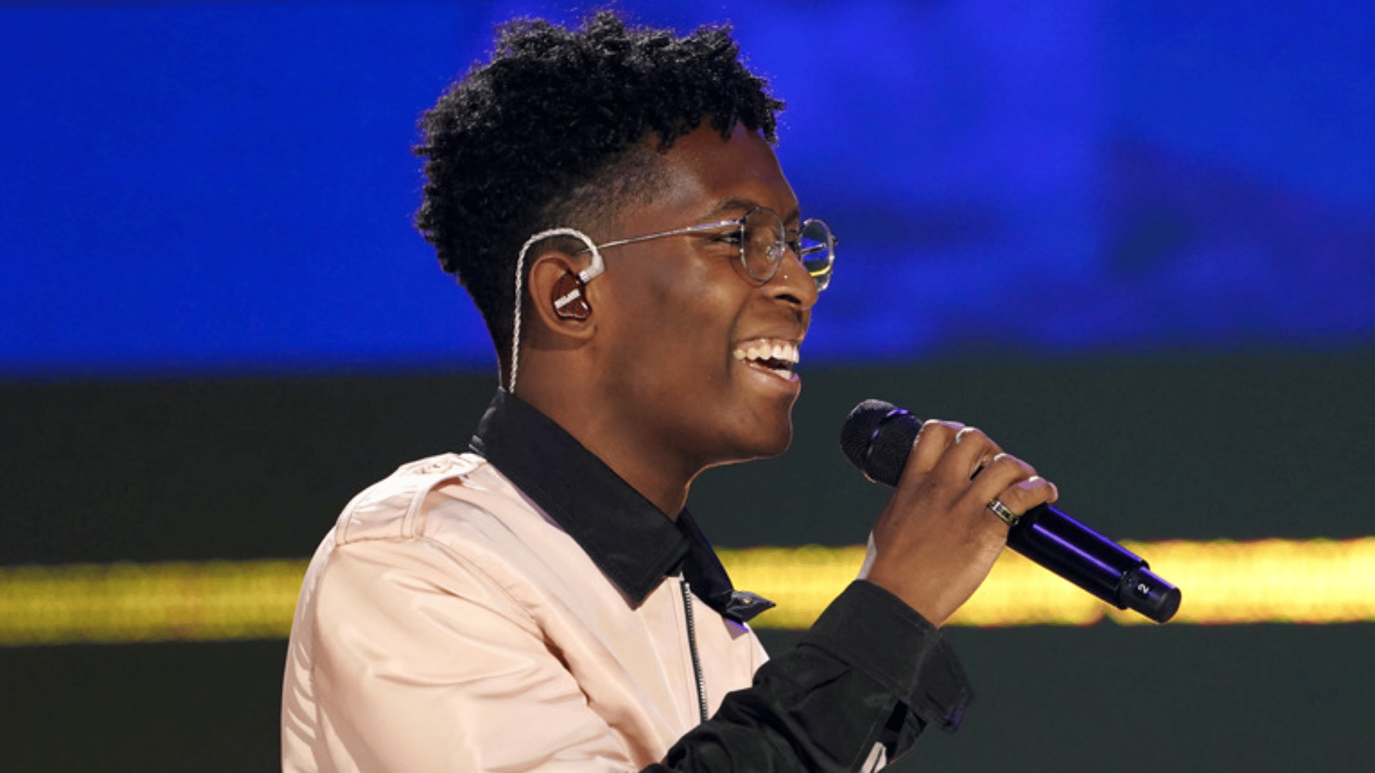 breland performing live on stage smiling while holding a microphone and wearing glasses and in ear monitors