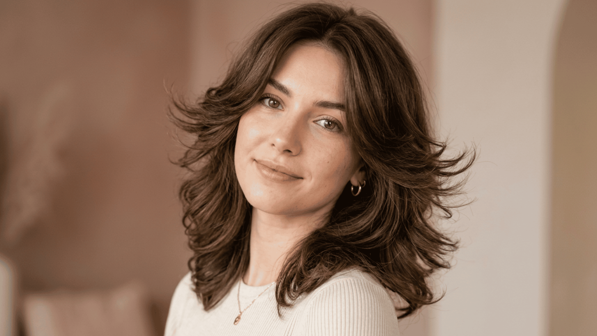 Woman with oblong face styled with butterfly cut layers and soft waves on warm background