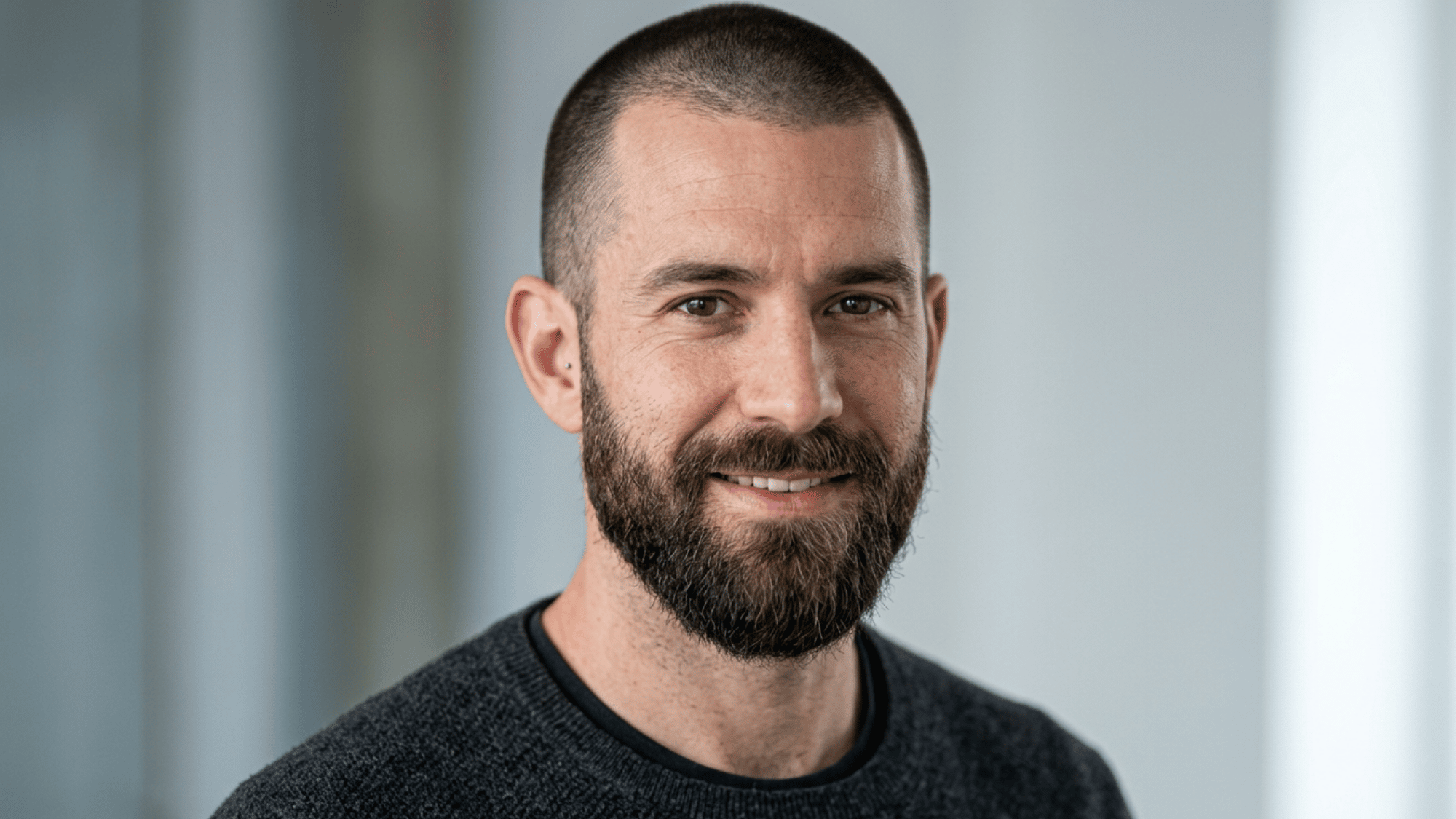 Man with oblong face showing buzz cut paired with full beard on grey background