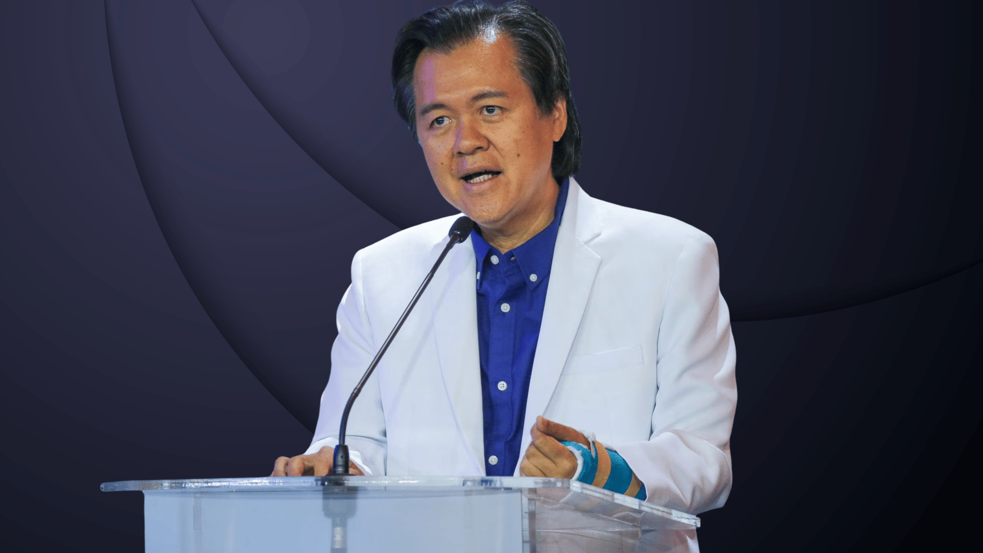Senator Willie Ong speaking at a podium in white blazer during an official public event in Philippines
