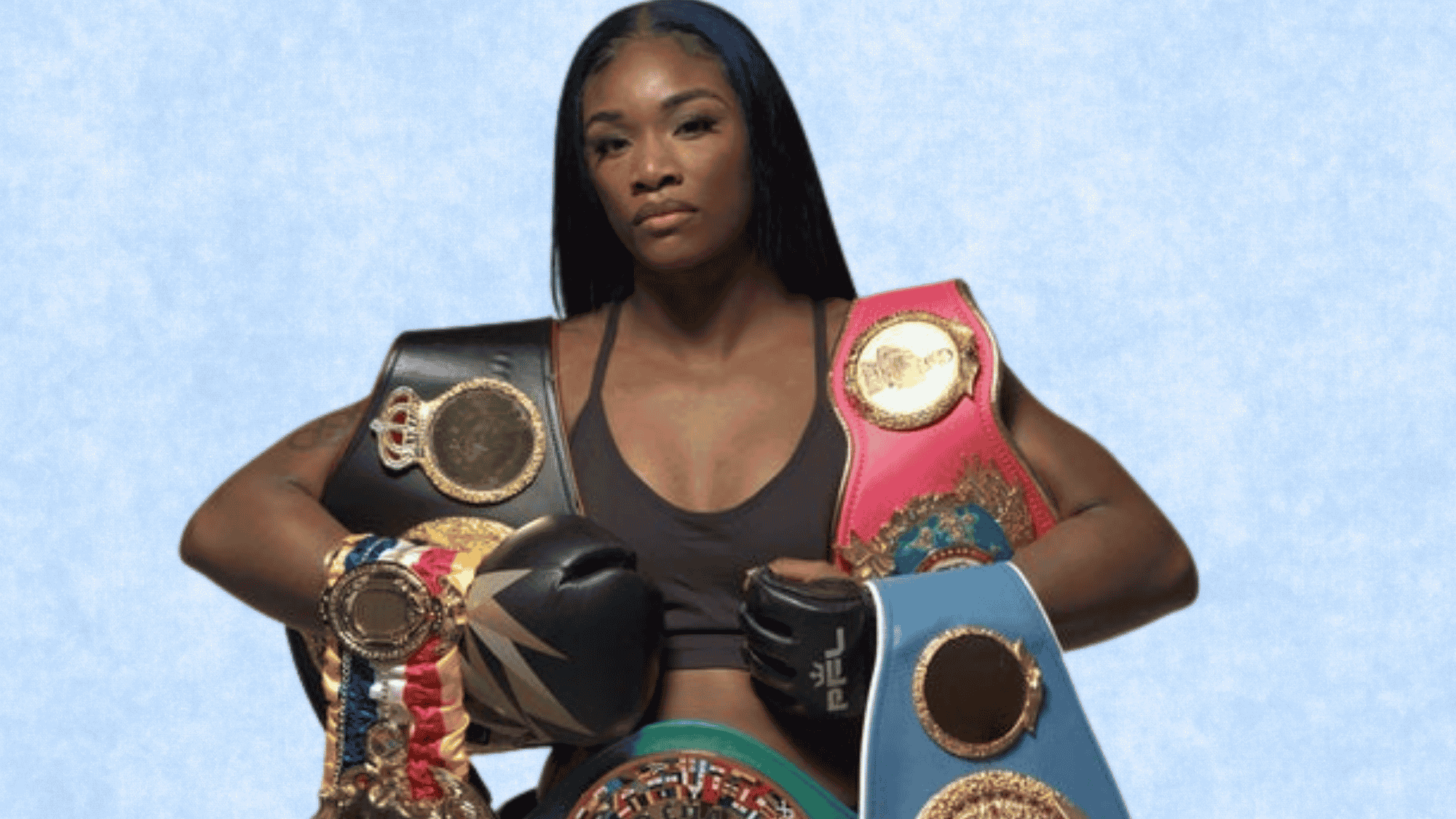 Claressa Shields smiling and holding up her championship belts and gold medals to showcase her career boxing achievements.