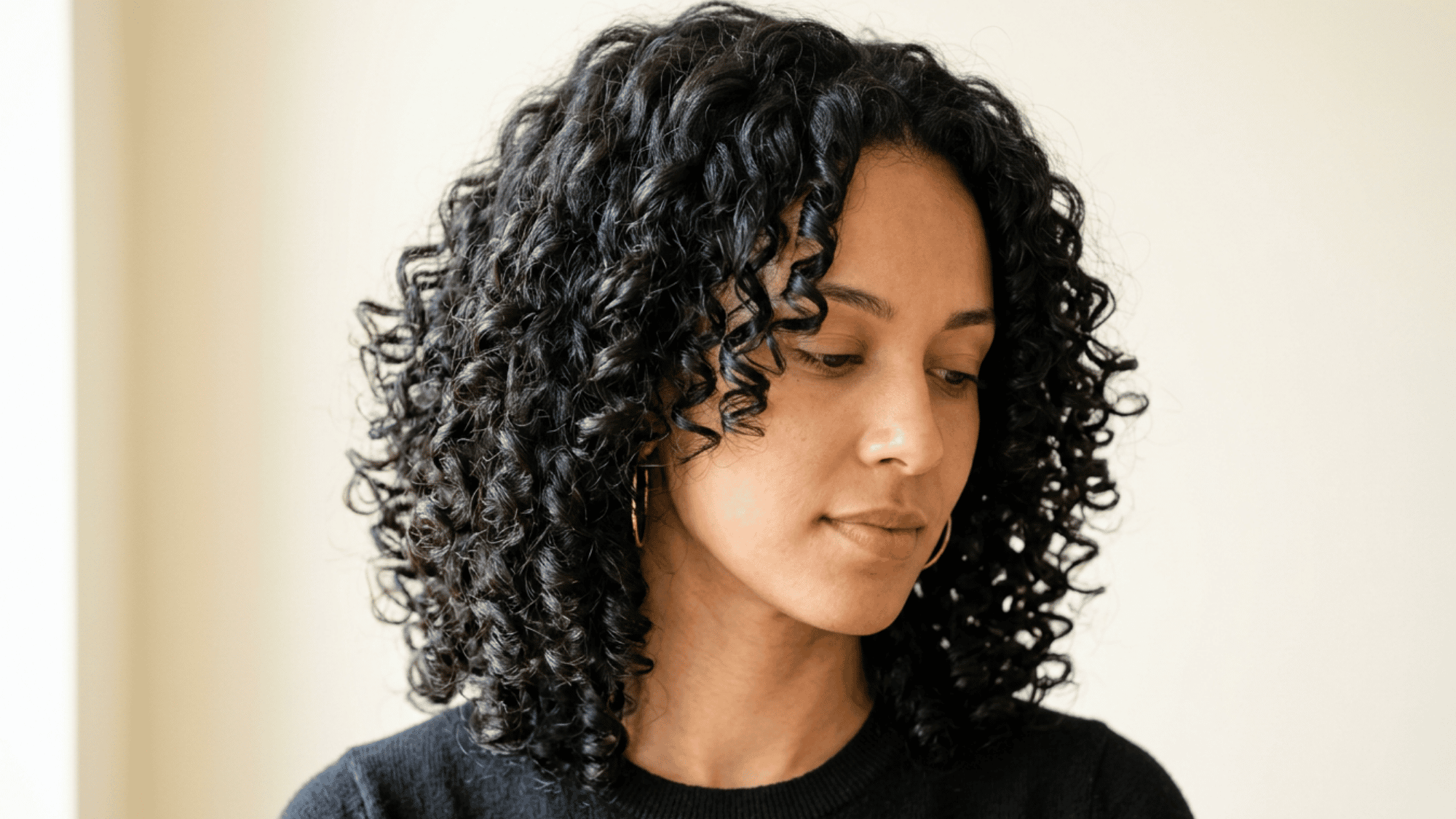 Woman with oblong face showing defined curly shoulder length cut on light background