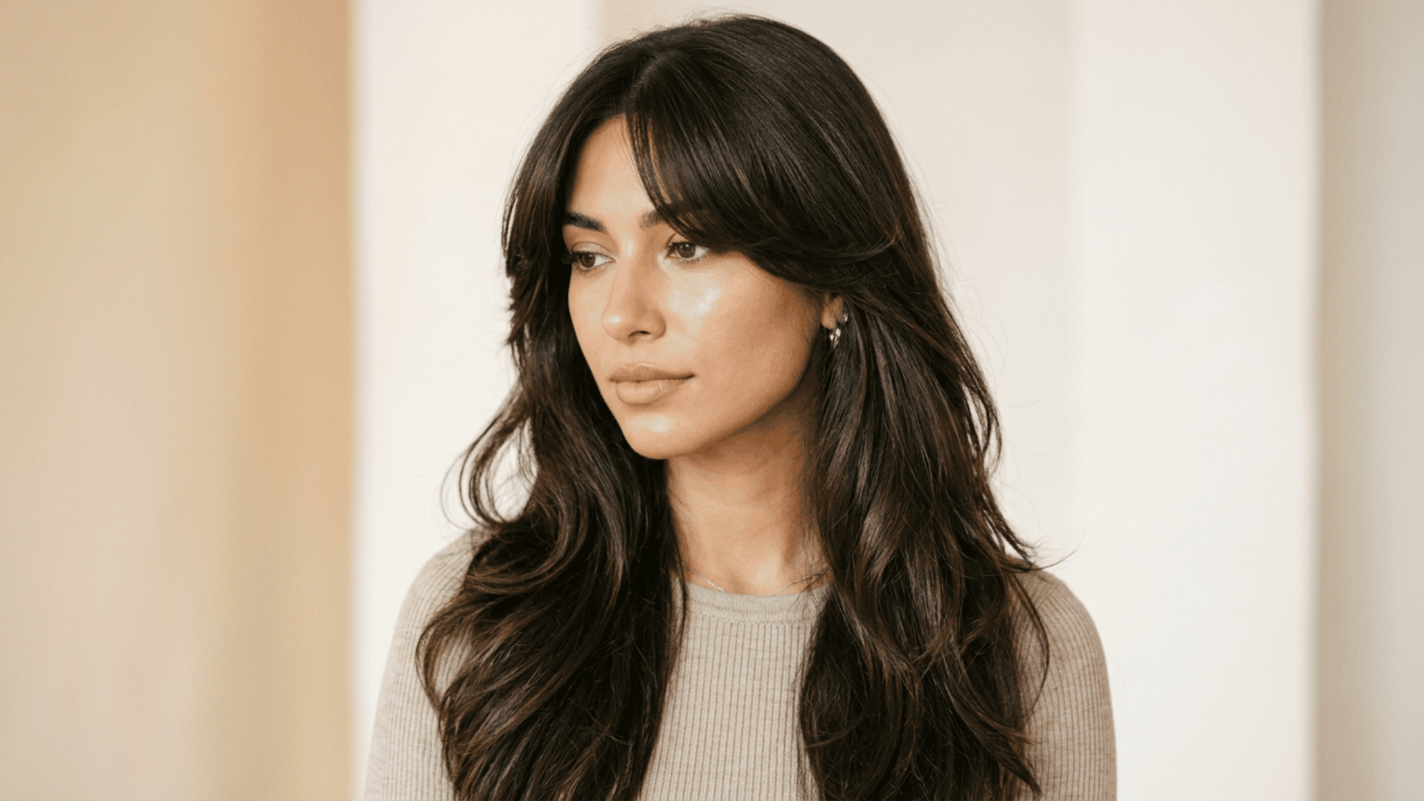 Woman with oblong face styled with curtain bangs and long wavy hair on warm background