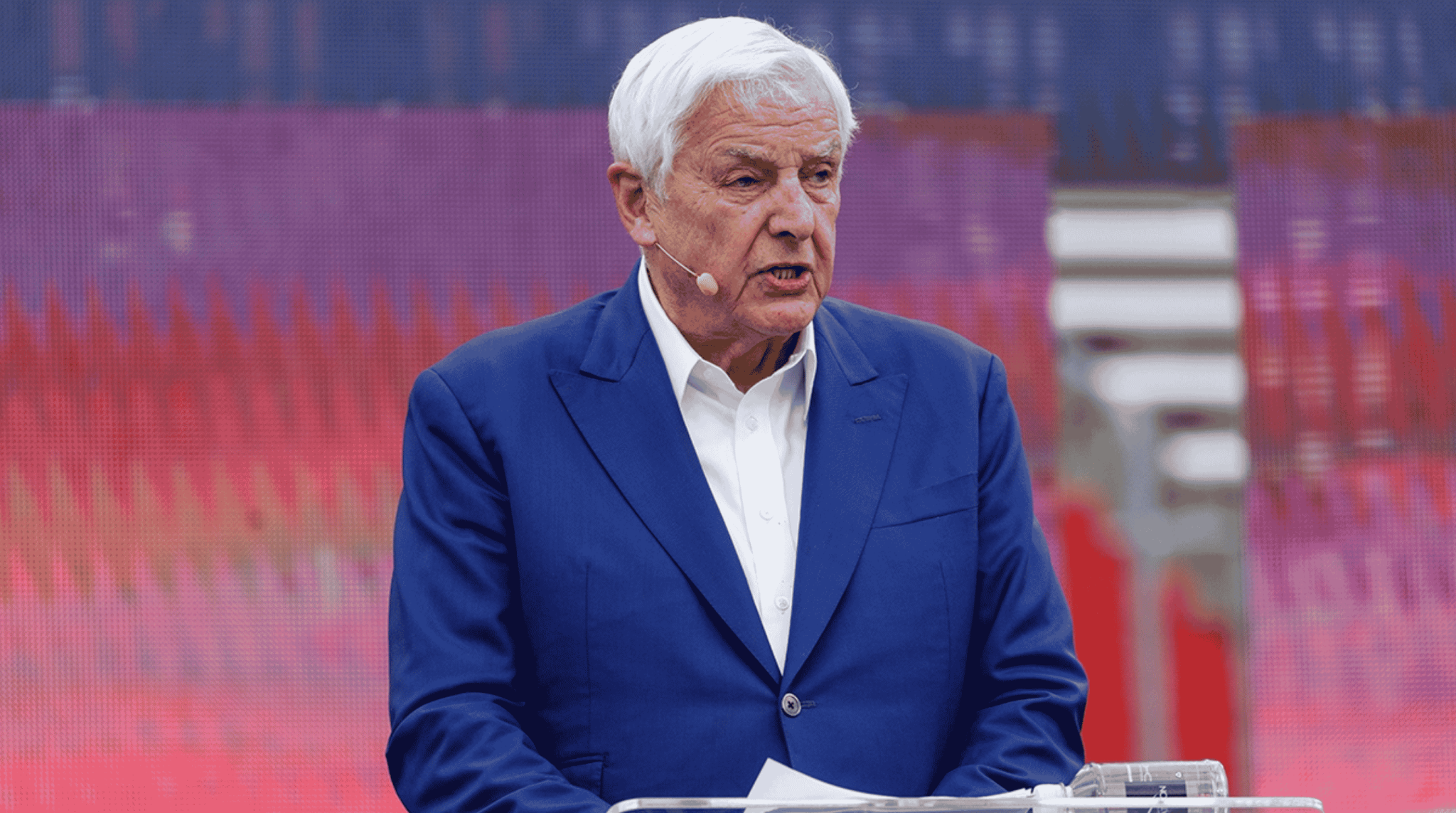 David Jeremiah speaking at a large event venue wearing a blue blazer and earpiece microphone