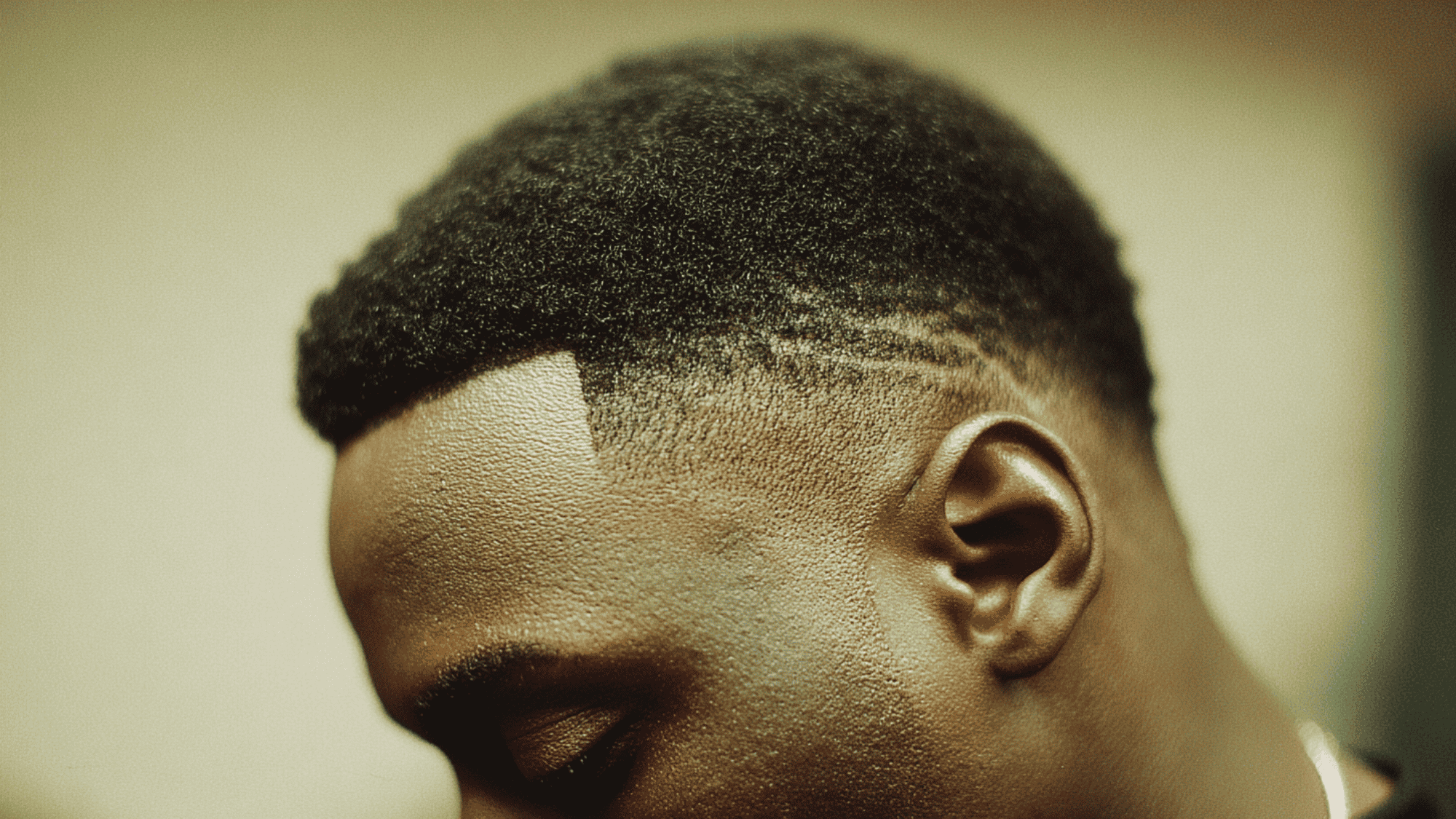 Drop fade black men curved line behind ear natural coily afro top side view portrait