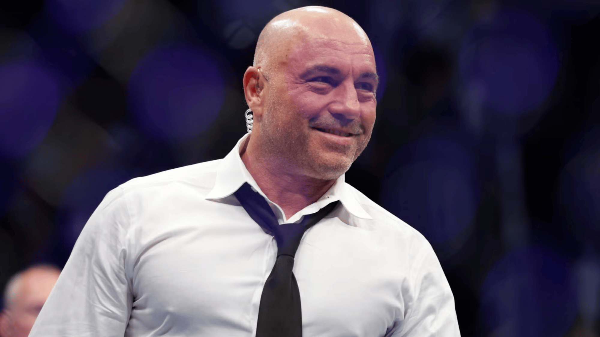 Joe Rogan smiling in a white shirt and black tie at a UFC event