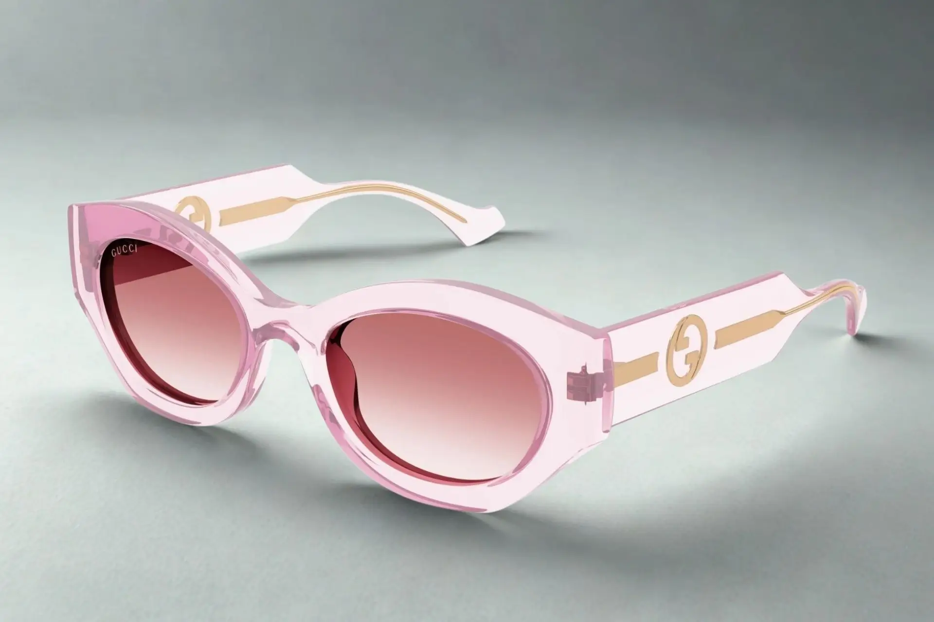 Pink sunglasses with gradient lenses on a grey surface in a minimalist setting
