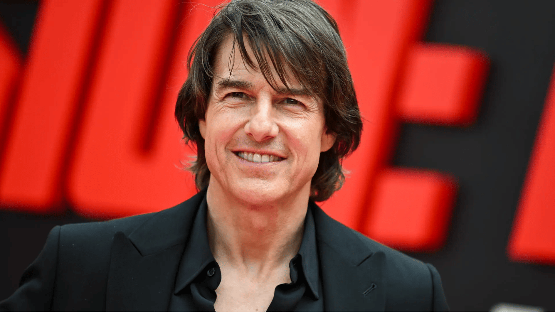 tom cruise smiling at a red carpet event wearing a black suit, showcasing his youthful appearance in 2026