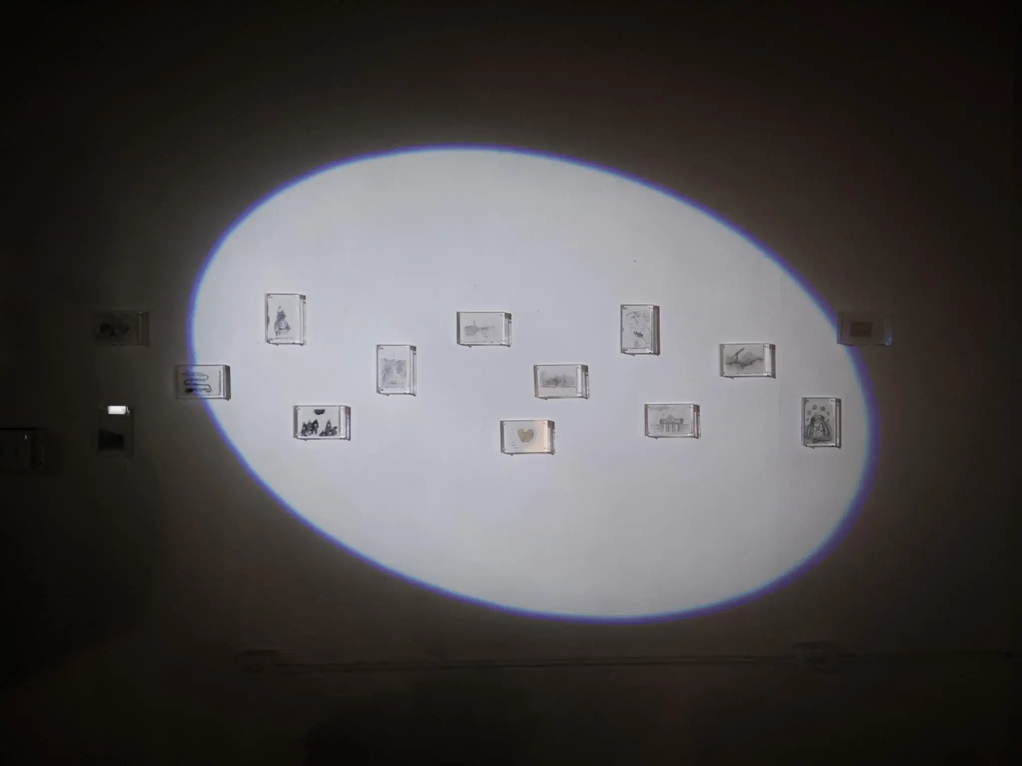 Small framed drawings on a dimly lit gallery wall with spotlight focus