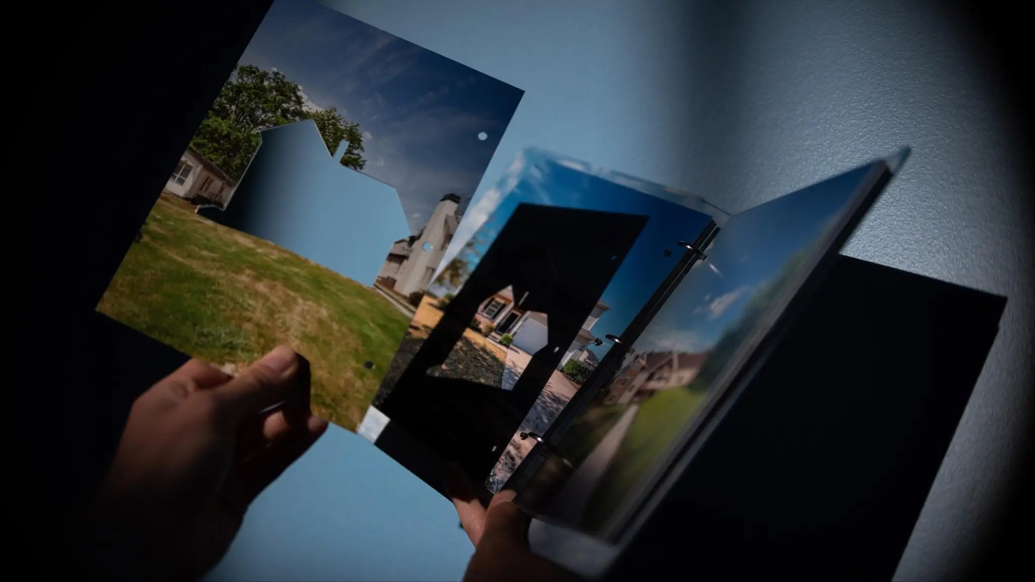 Person holding a photo album with outdoor house images under low light