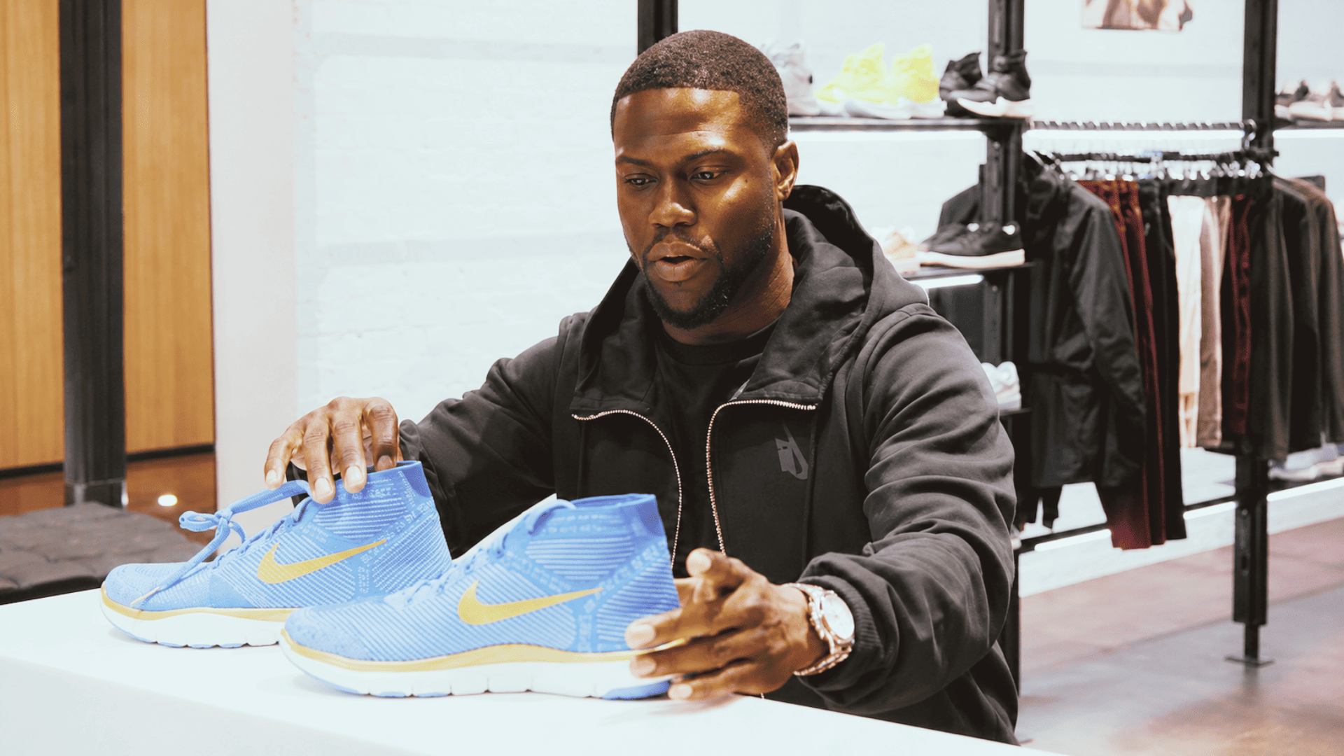 kevin hart looking at nike shoes inside a sports store surrounded by footwear displays
