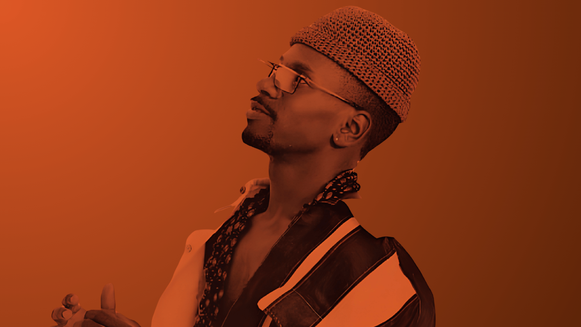 Side-profile portrait of larry heard in patterned cap and glasses under warm orange lighting.