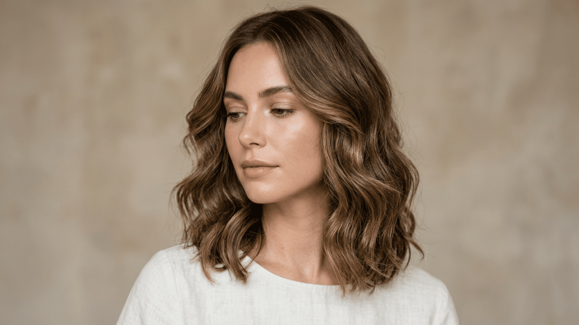 Woman with oblong face styled with wavy long bob on warm natural indoor background