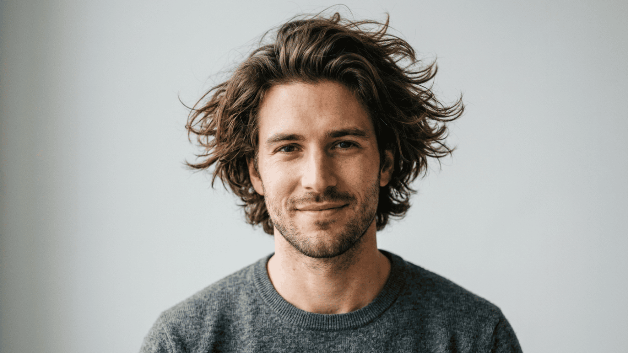 Man with oblong face styled with messy textured wavy hair on light background