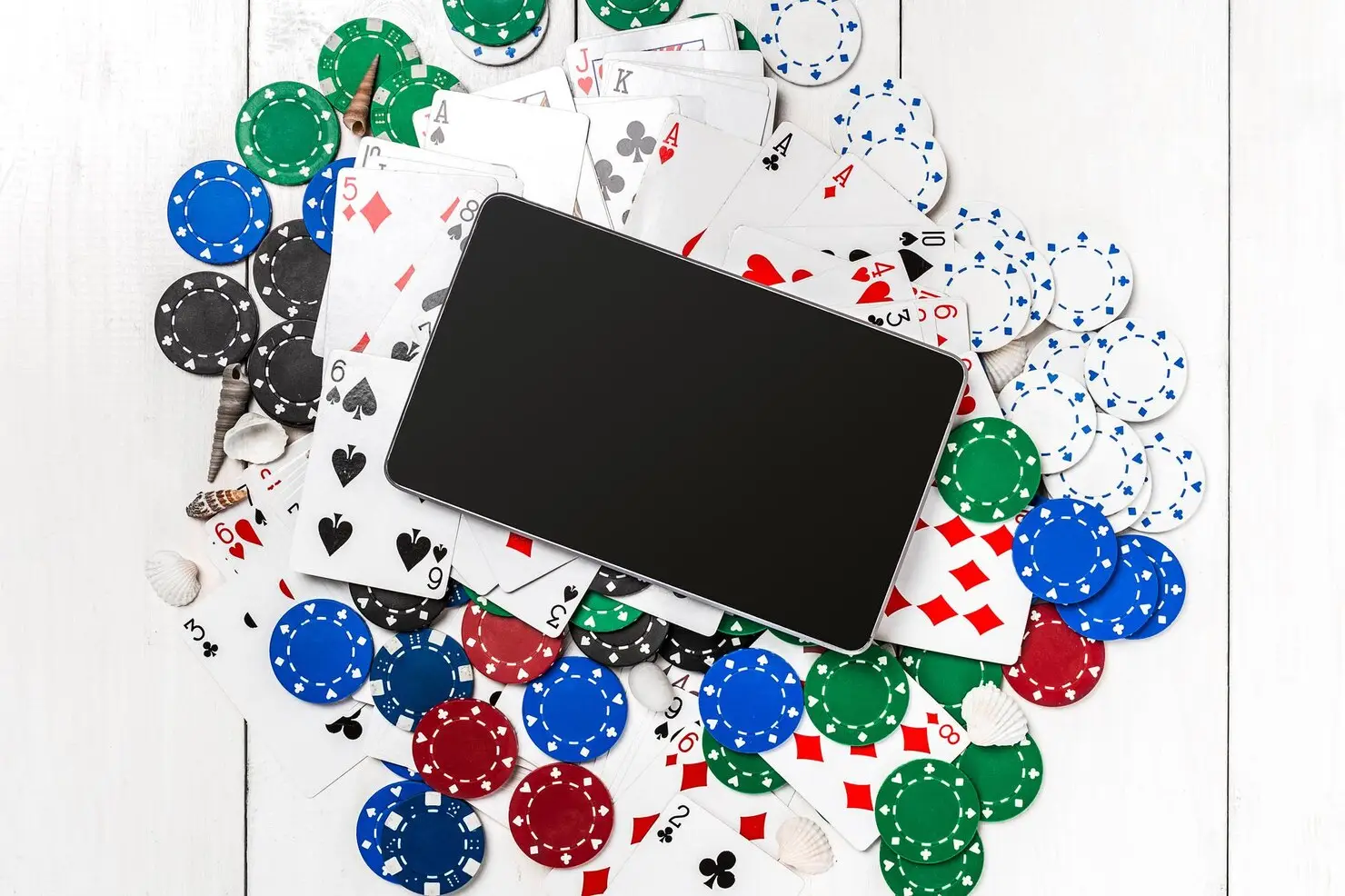 Tablet surrounded by playing cards and colorful poker chips on a white wooden surface