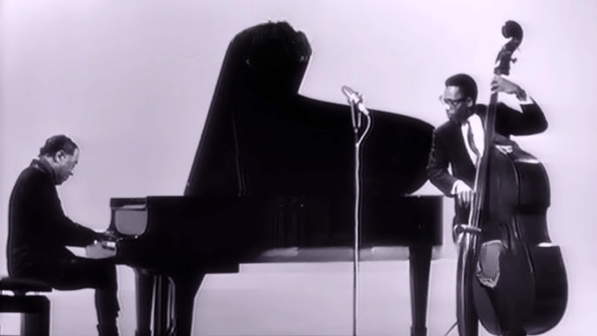 Duke Ellington at grand piano performing Mood Indigo with bassist in black and white archival photograph