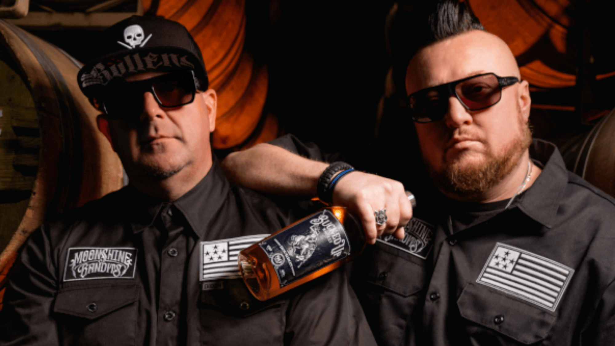 moonshine bandits members bird and tex posing in black outfits inside a whiskey barrel storage room