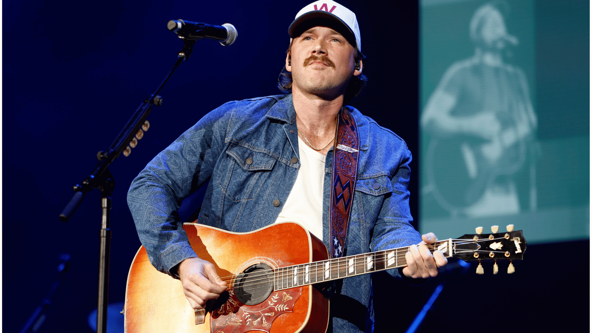 Morgan Wallen in a striking blue jacket performing on stage with his guitar