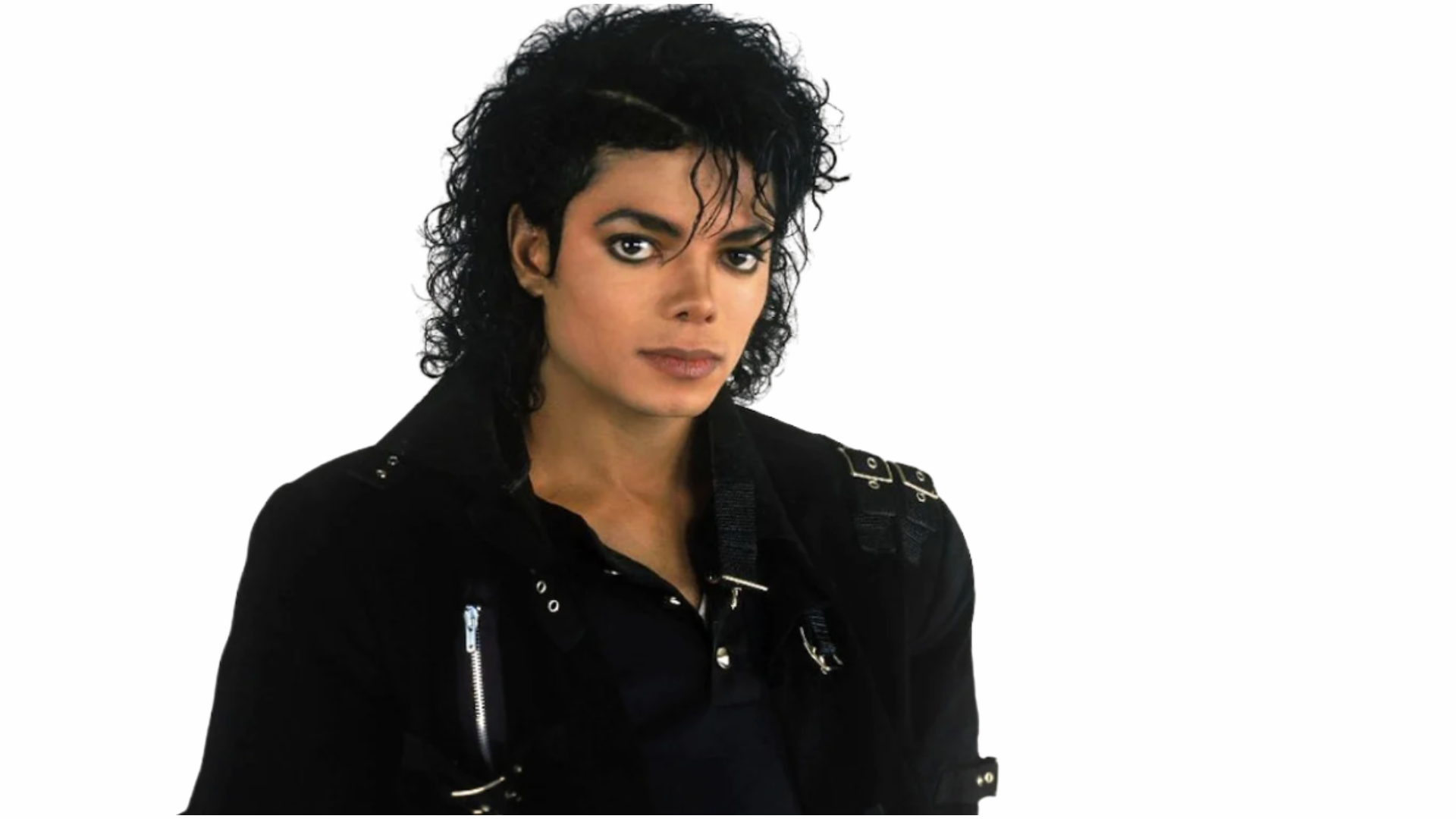 person with curly black hair wearing a black jacket and looking forward against a plain light background