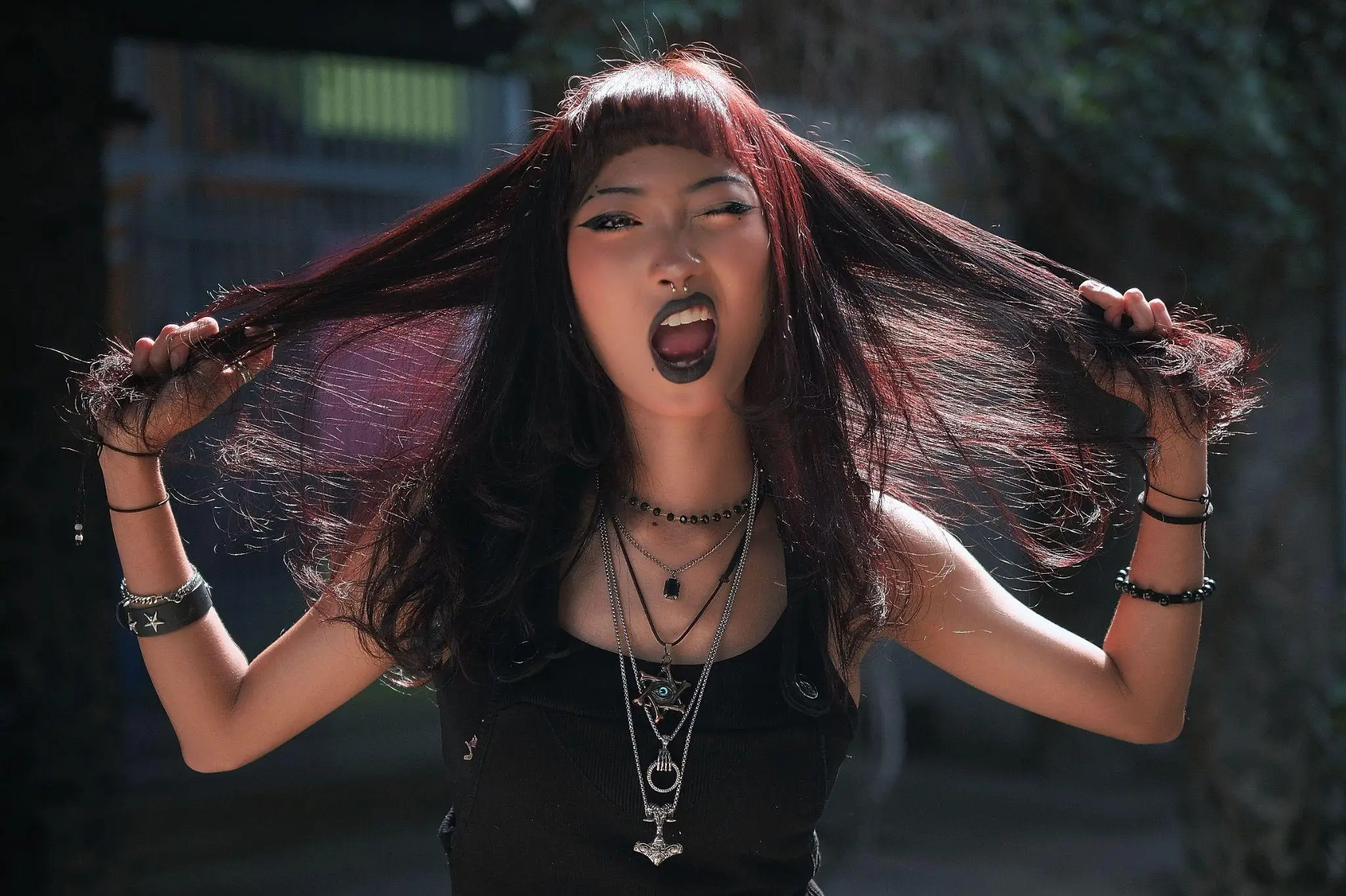 Goth woman with dark makeup and jewelry pulling hair outdoors in moody lighting