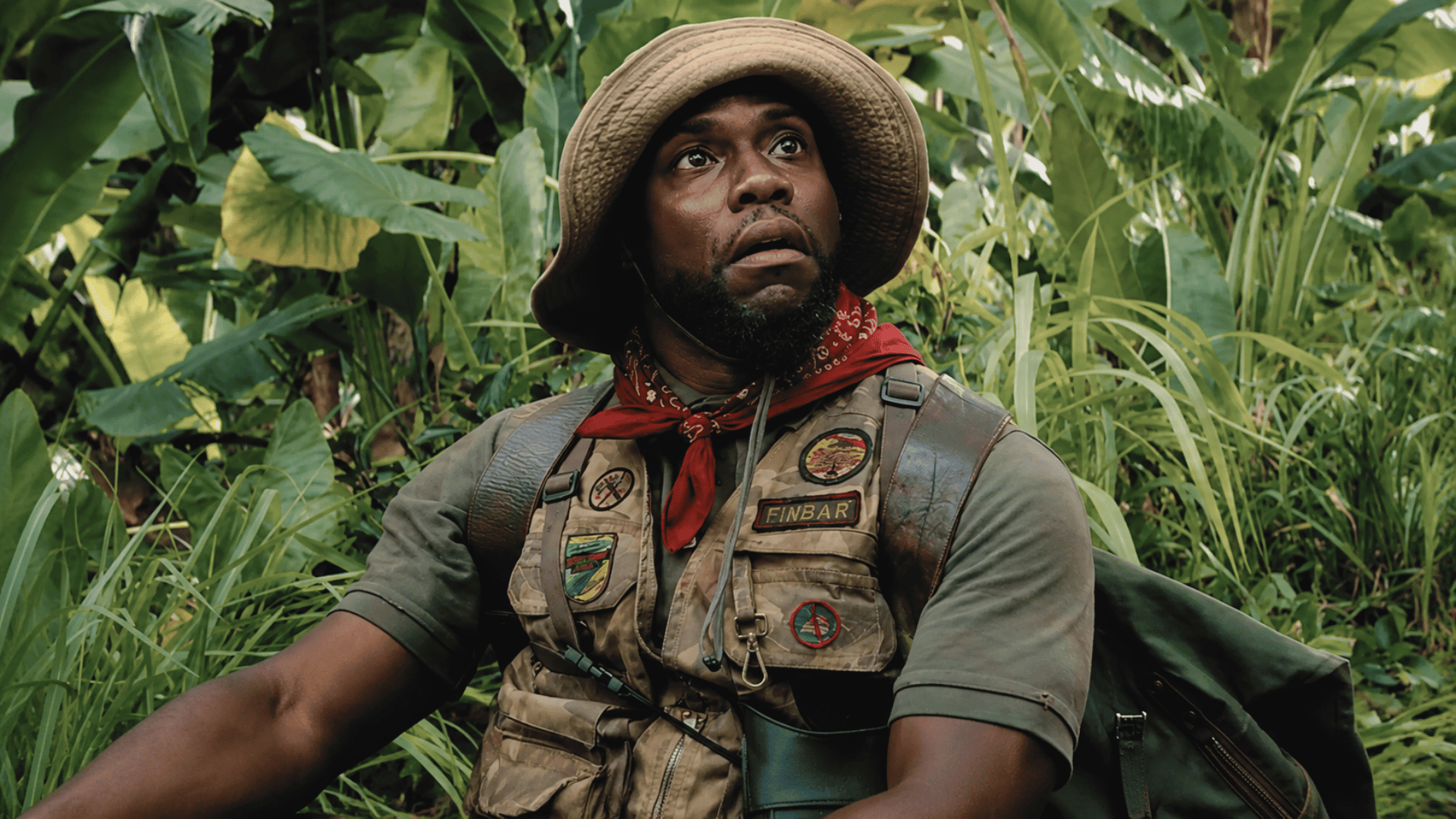 scene from Jumanji kevin hart sitting in a tropical jungle looking upward with a surprised expression