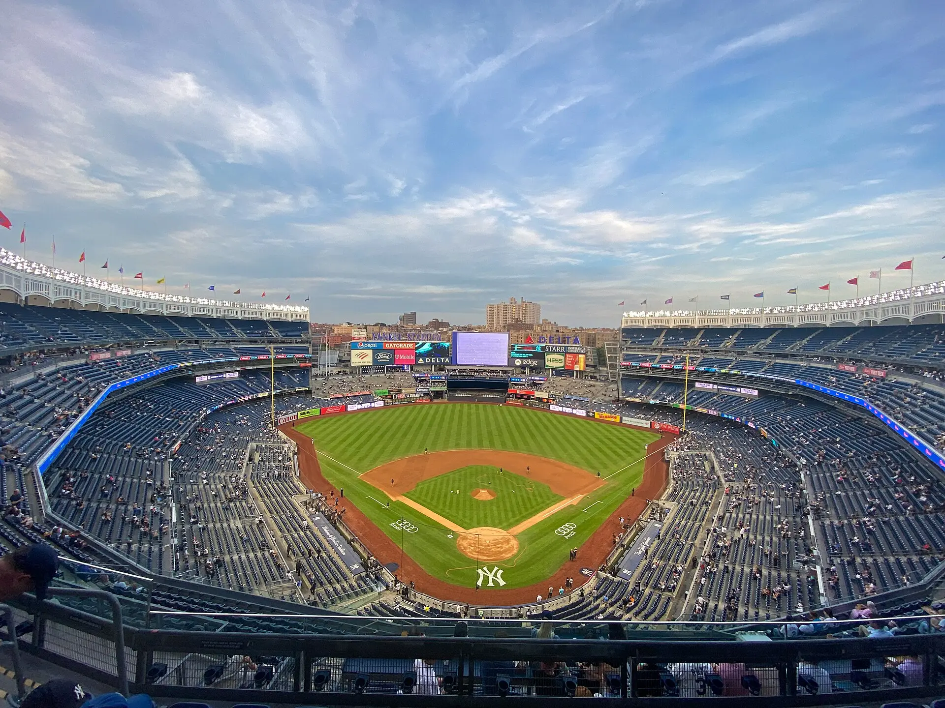 Wide-angle view of baseball stadium with green field and partially filled stands under cloudy sky