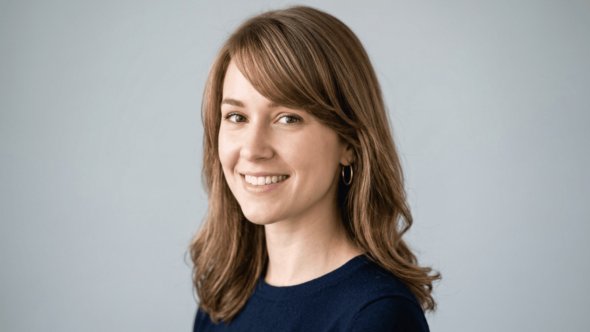 Woman with oblong face styled with side swept bangs and layered hair on grey background