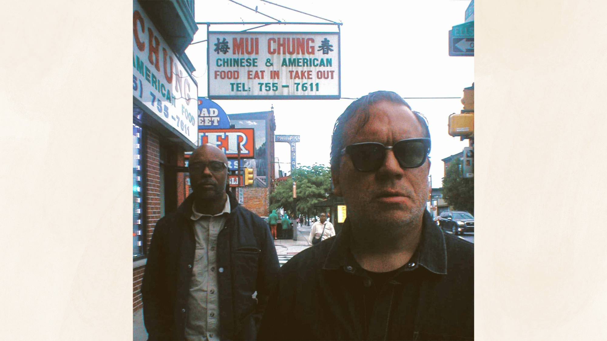street photograph of two men wearing sunglasses standing beneath vintage restaurant signs in urban neighborhood