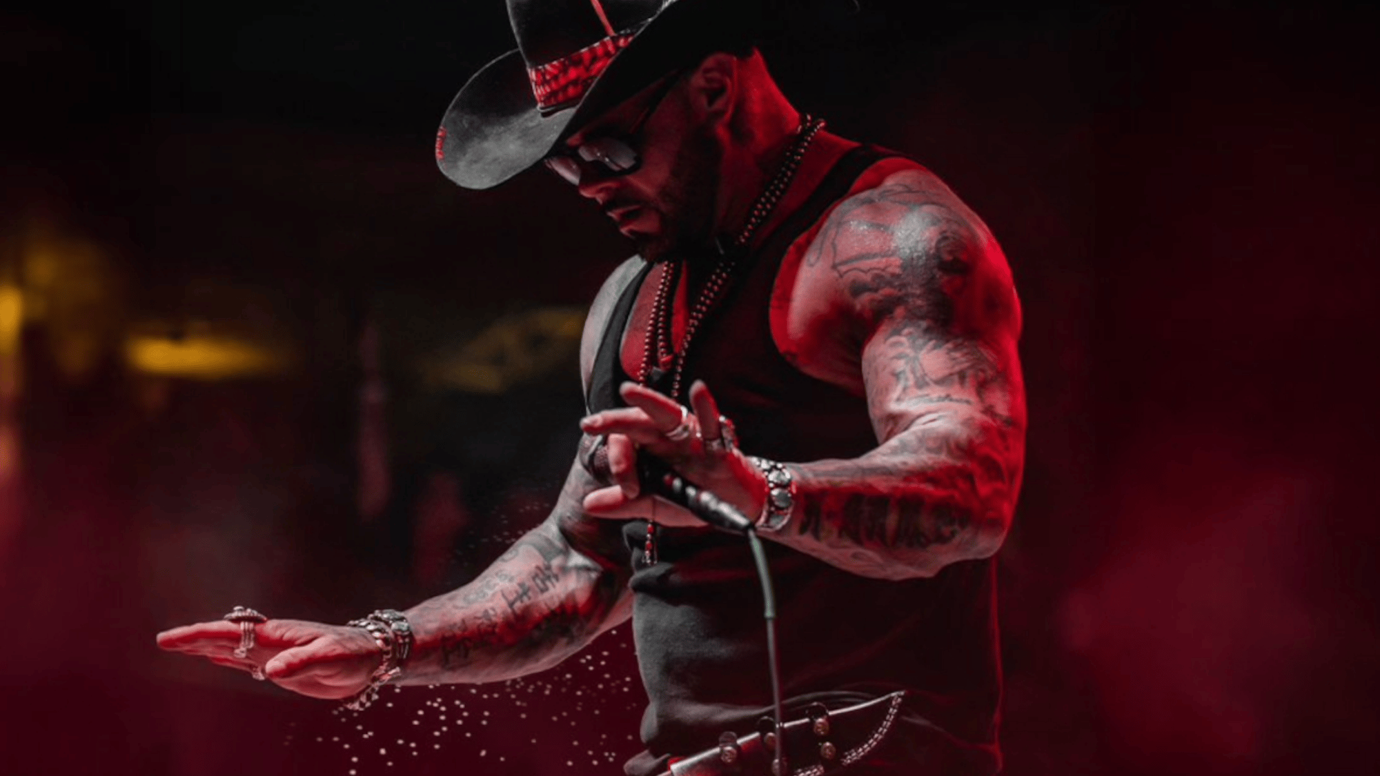 country rap artist performing on stage wearing a cowboy hat and black outfit under dramatic red lighting