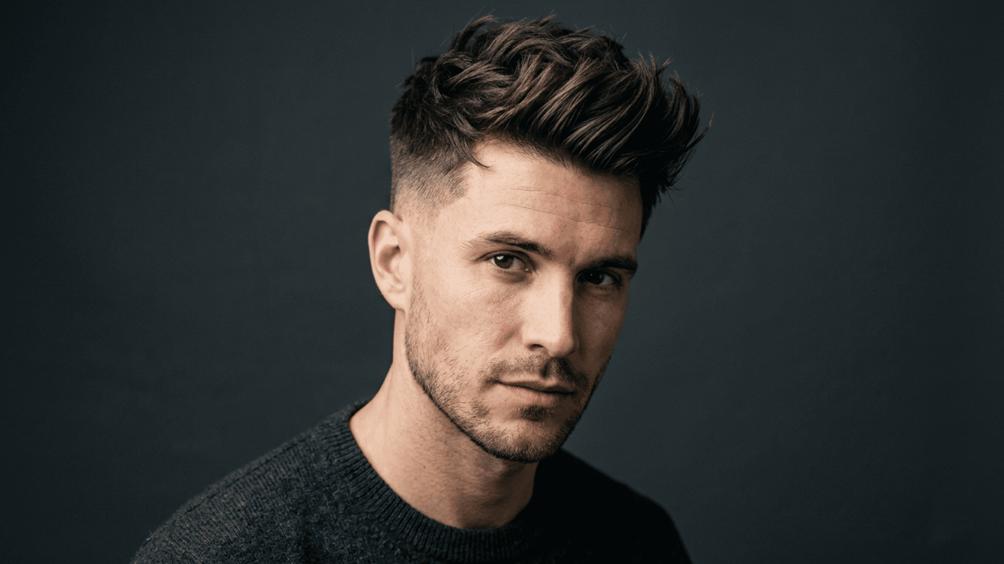 Man with oblong face styled with textured crop and short faded sides on dark background