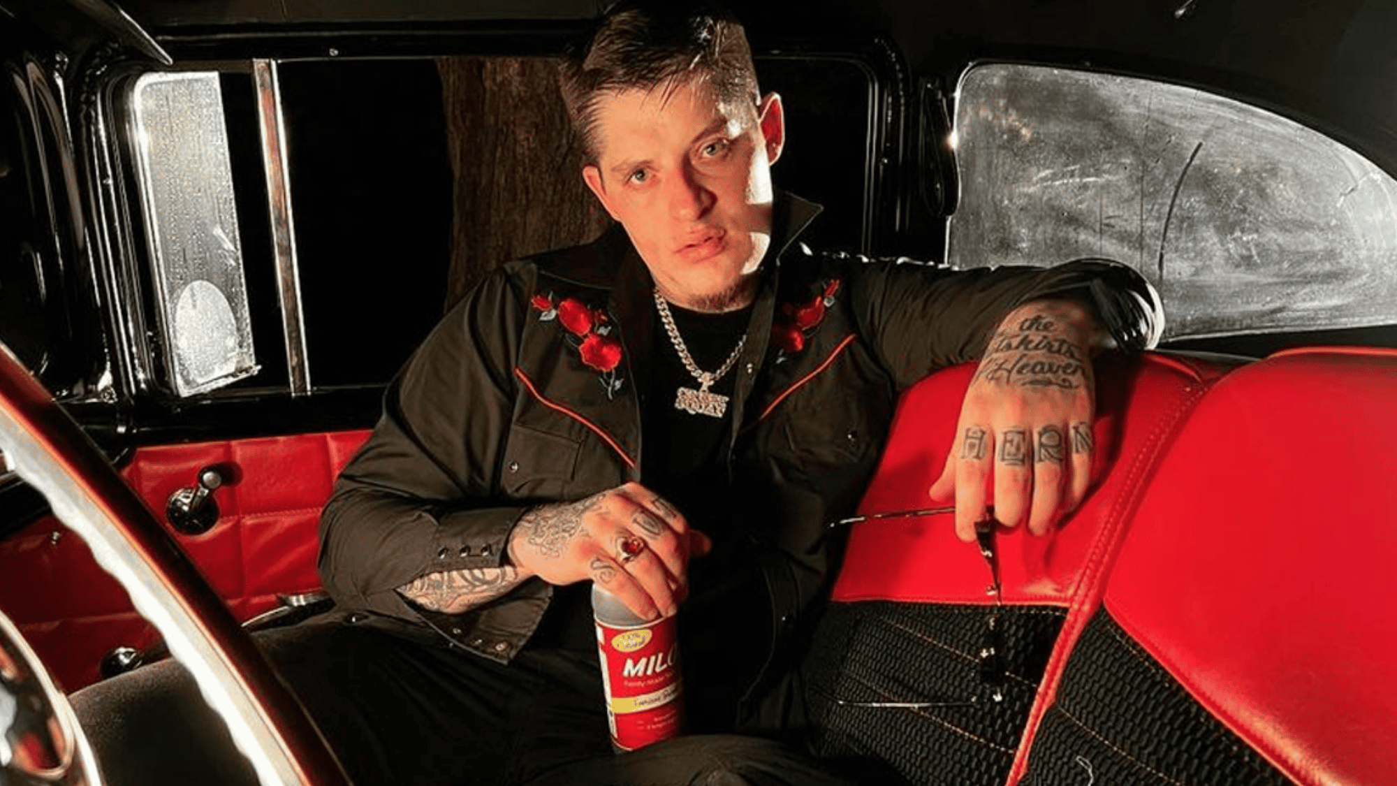 upchurch sitting inside a vintage truck with red seats wearing black western clothing and silver chains