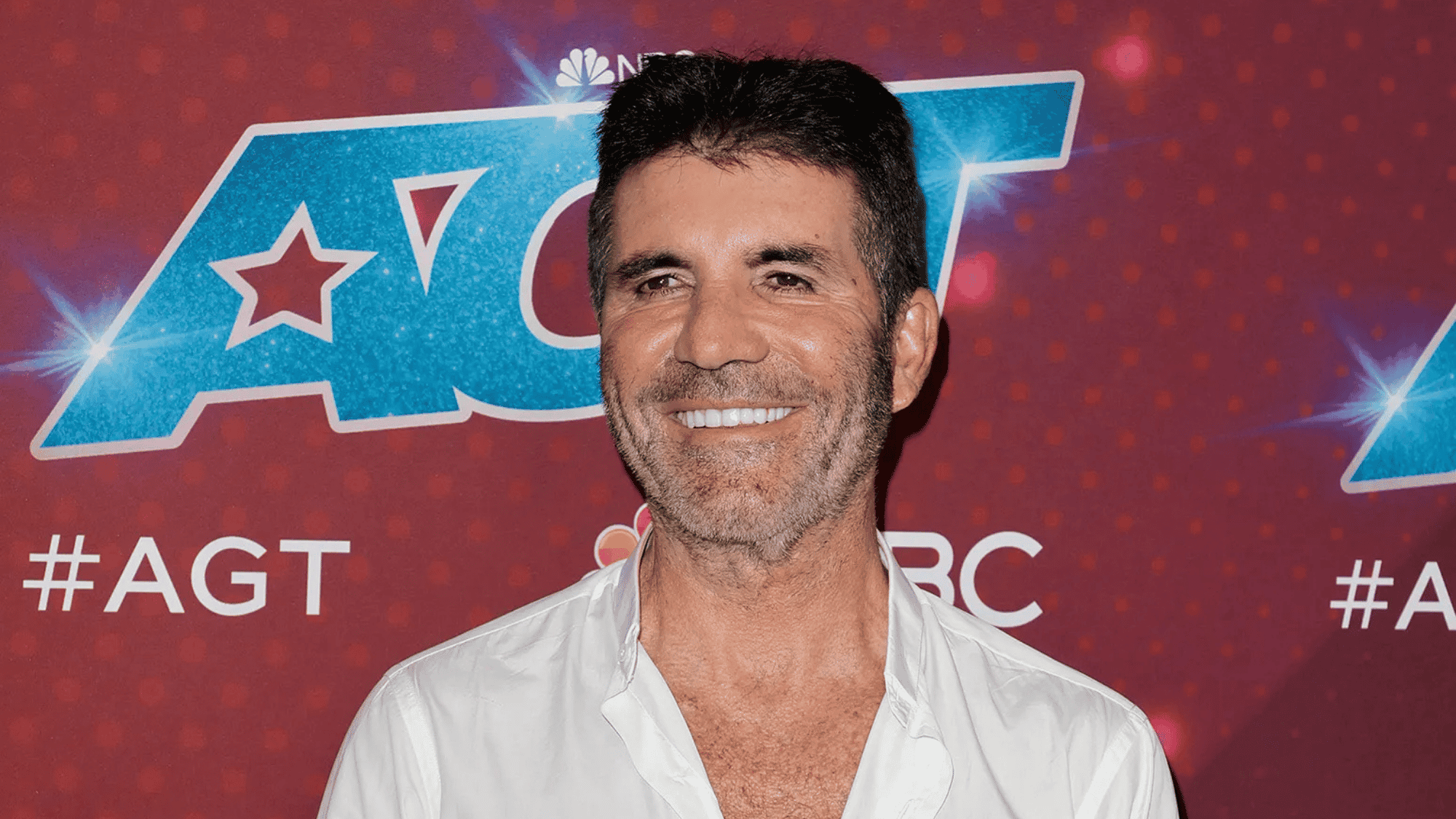 Simon Cowell smiling in white shirt at America's Got Talent AGT red carpet
