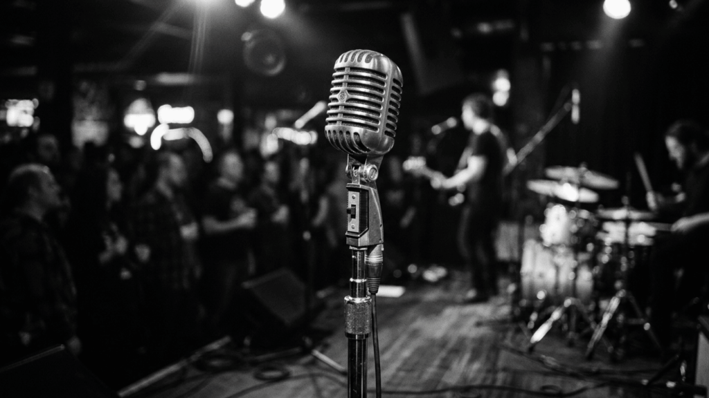 Vintage microphone on a stage with a blurred live band and audience during a karaoke night performance.