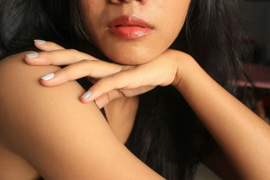 Close-up of a woman's face and hands with painted nails in soft lighting