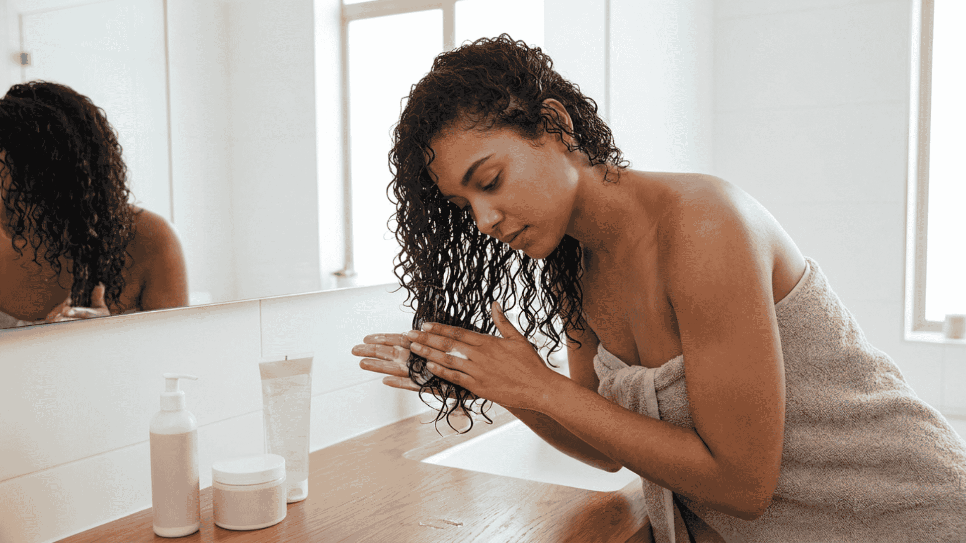 woman applying styling products to sections of soaking wet curly hair