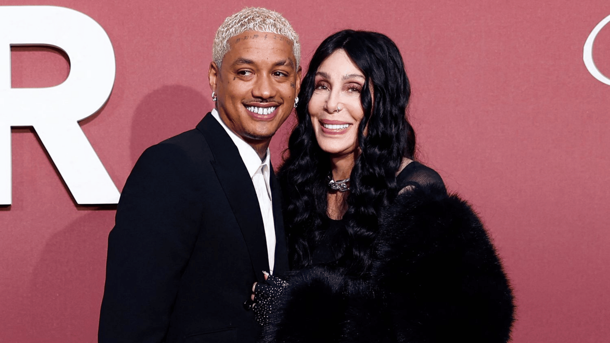 Singer and partner posing together on a red carpet with a pink backdrop