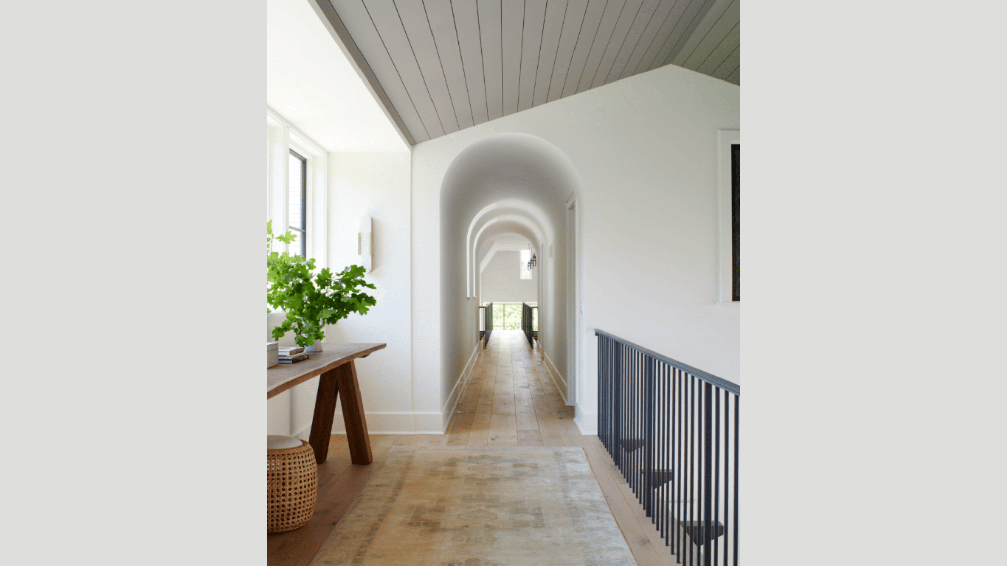 bright arched hallway with wood flooring, black railings, natural light, and minimalist decor creating an elegant transition space.