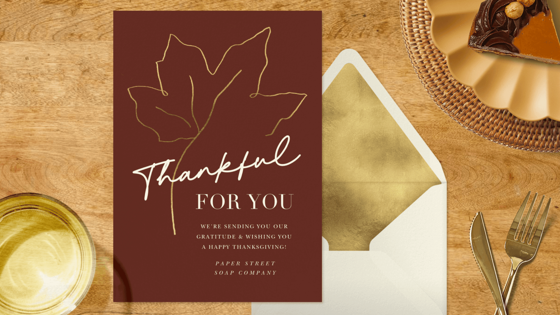 brown thanksgiving card reading thankful for you beside an open envelope on a wooden table with a place setting
