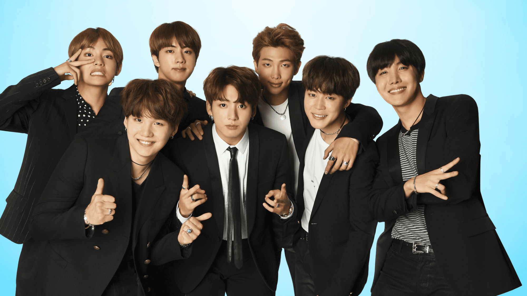 BTS members posing together in black outfits, smiling and making hand gestures during an official group promotional photoshoot.