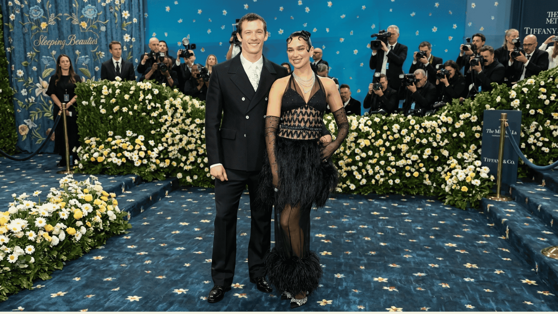Couple posing on a floral blue carpet at a red carpet event with photographers behind them