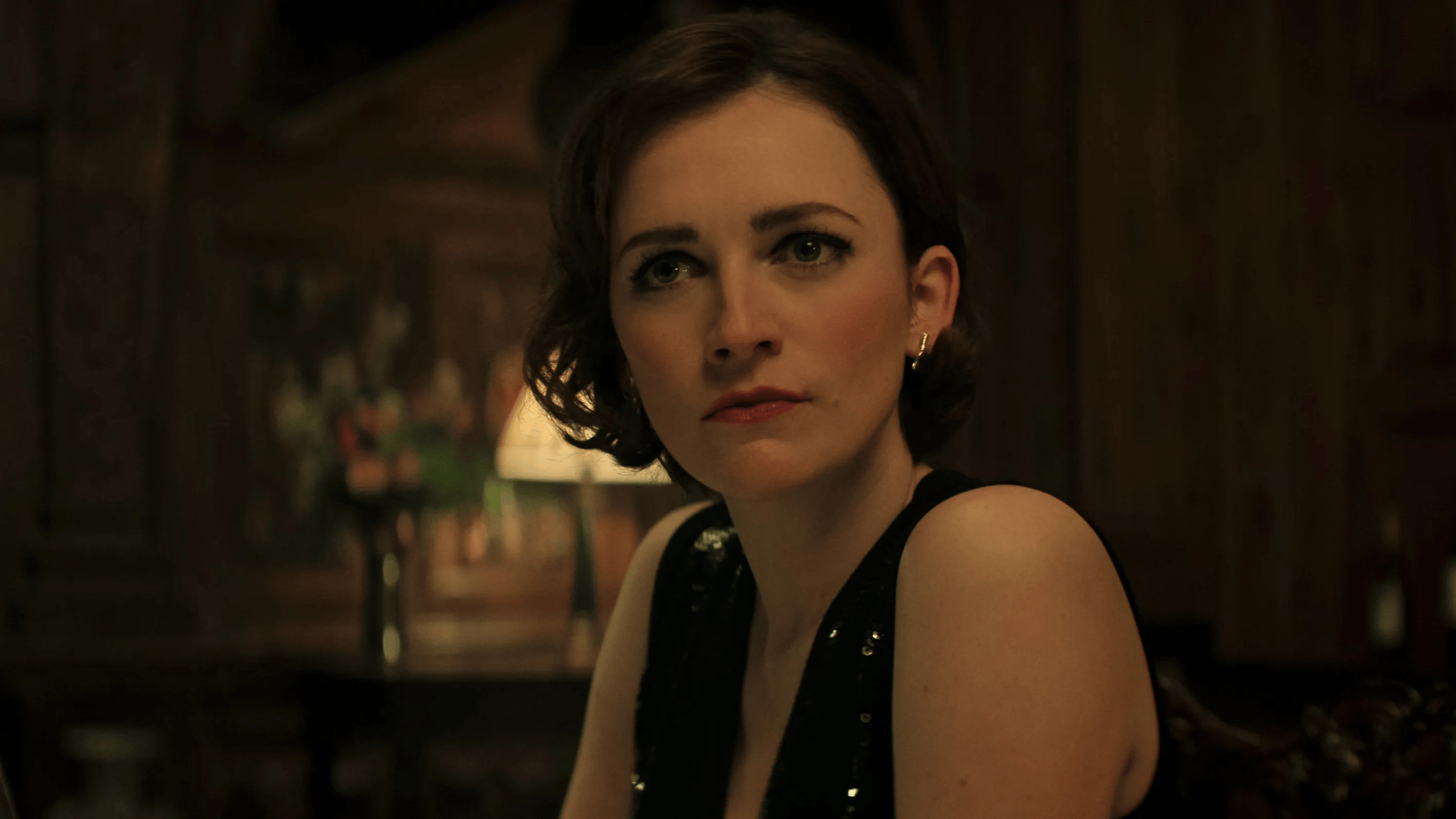 Woman in black dress sitting in a dark, warm-toned room