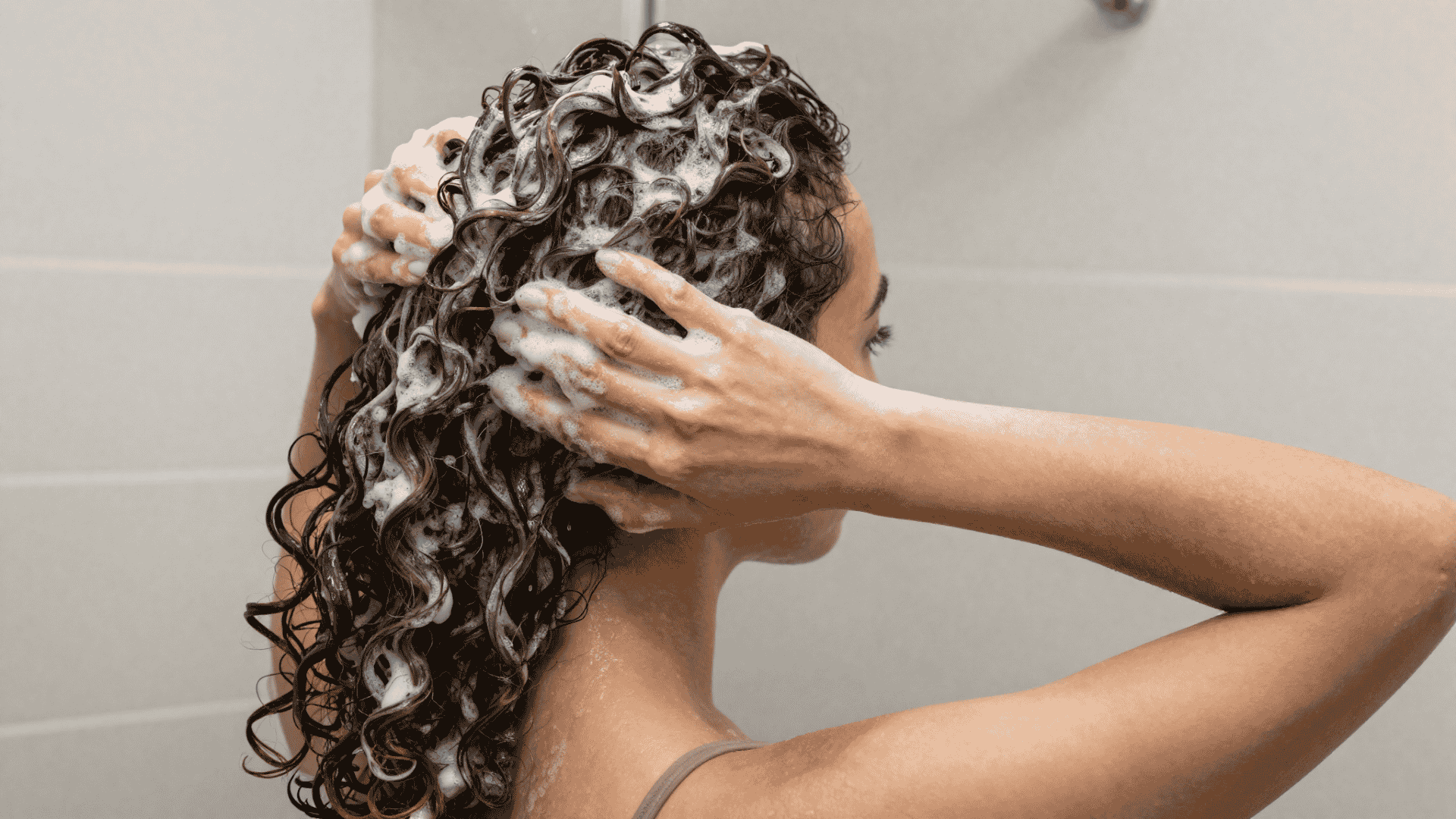woman gently massaging shampoo into the roots of her wet curly hair