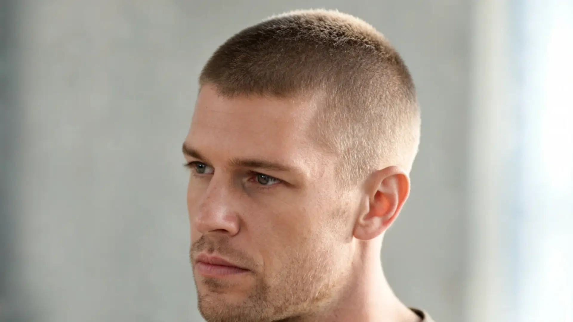 close up portrait of a man with a short brown buzz cut and faded sides against a light gray background