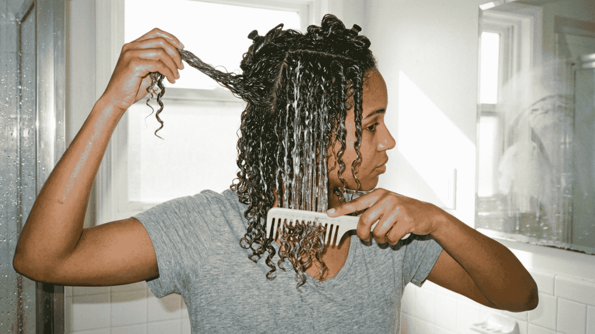woman conditioning and detangling wet curly hair with a wide tooth comb