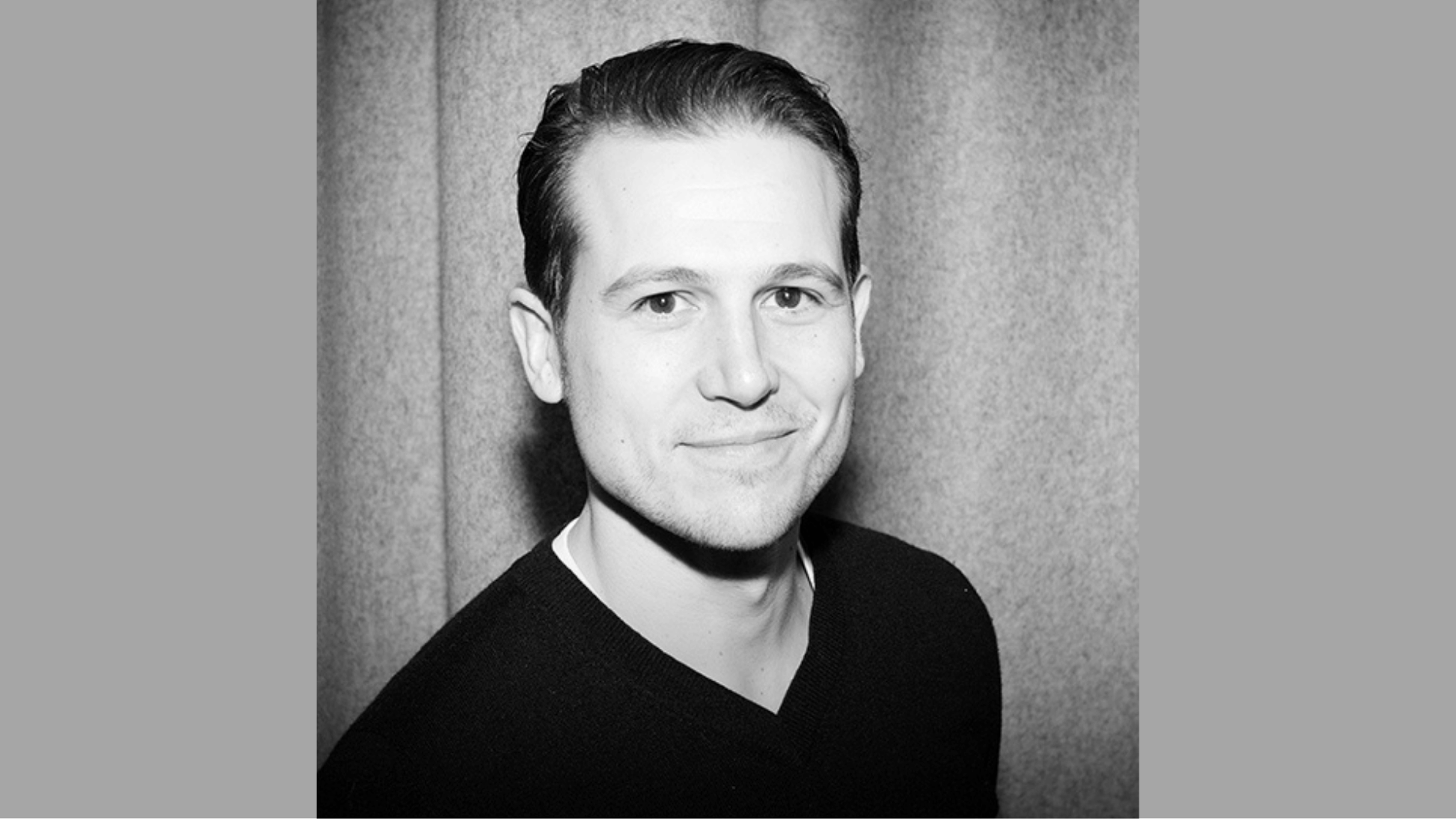 black-and-white headshot of a smiling man with neatly styled dark hair, wearing a dark V-neck sweater