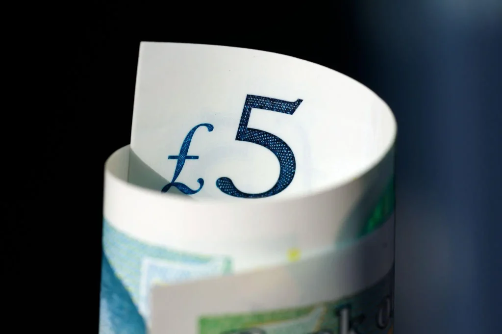 Close-up of rolled five-pound note with focus on currency symbol against dark background
