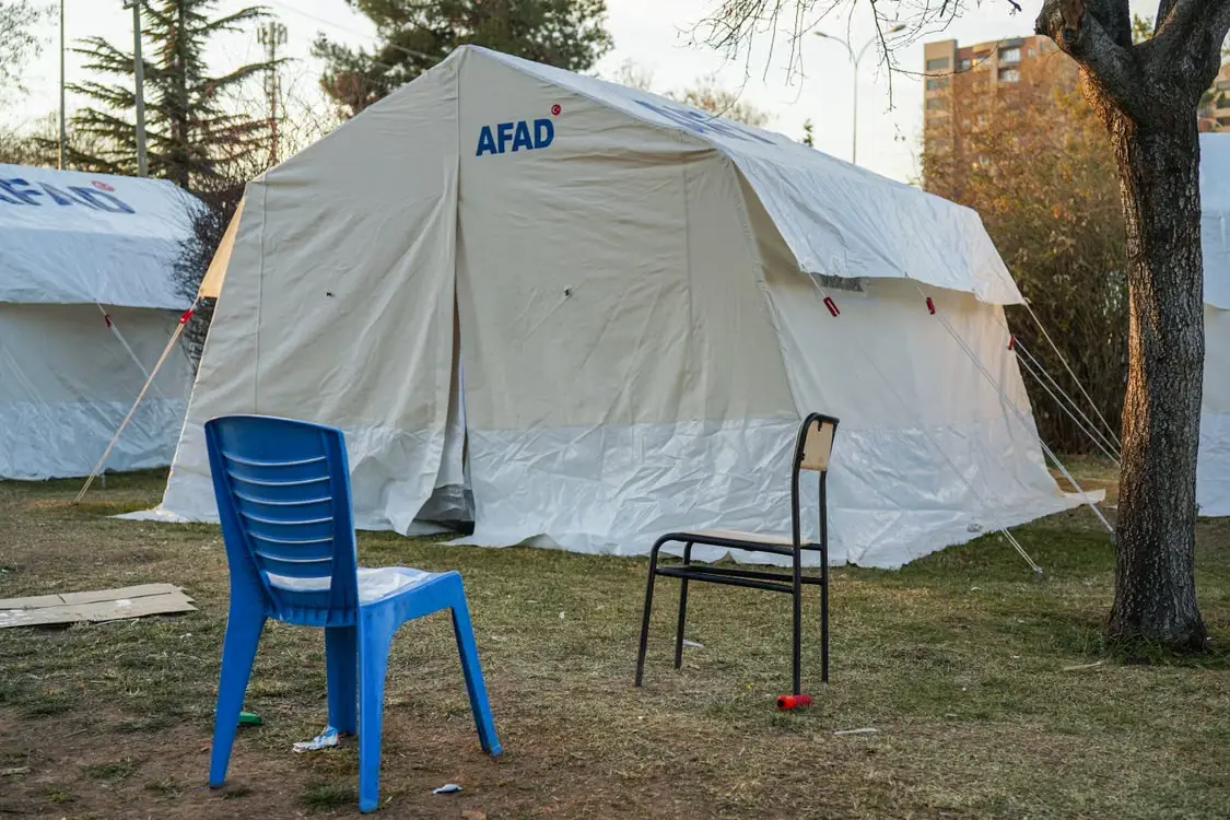 Camping tent in grassy area with blue and black chairs nearby