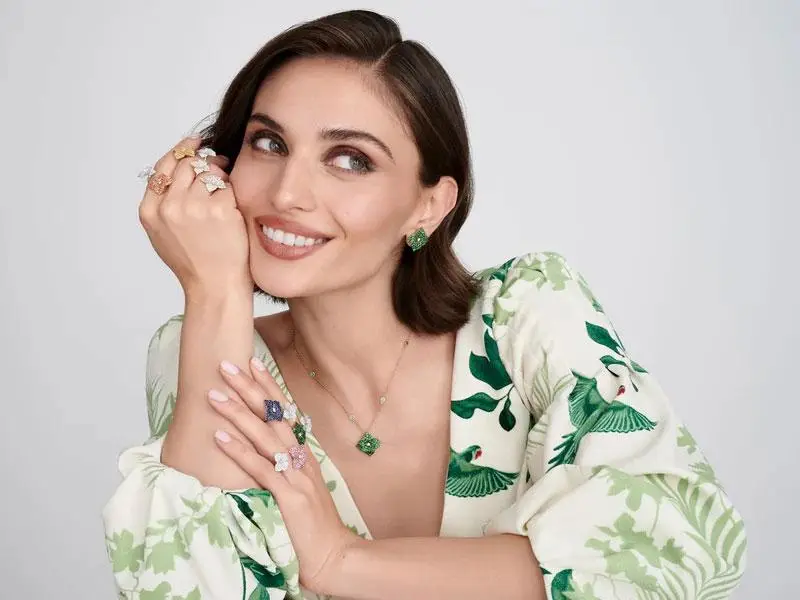 Woman wearing green and white floral dress with multiple gemstone rings and matching earrings